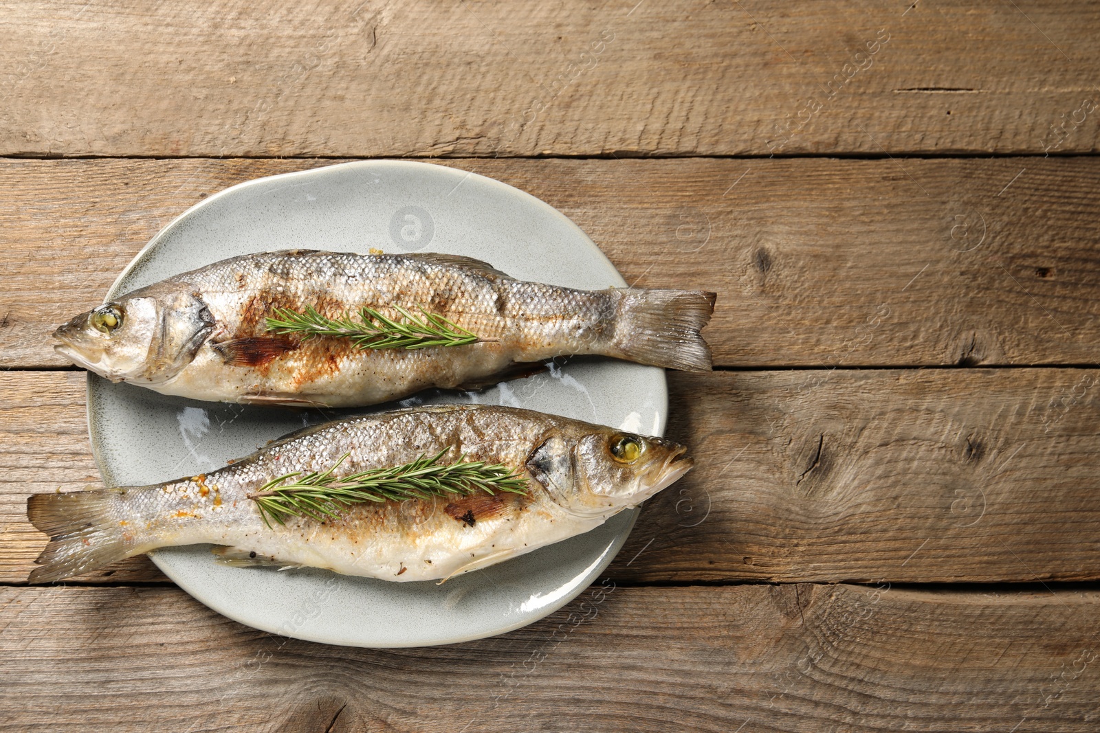 Photo of Delicious baked fish and rosemary on wooden table, top view. Space for text