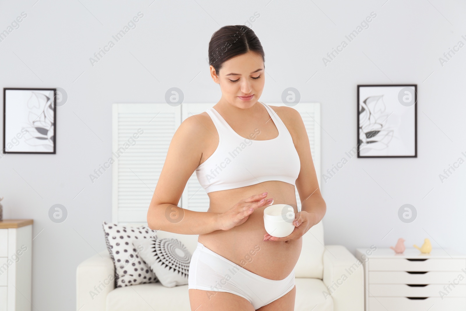 Photo of Pregnant woman holding body cream at home