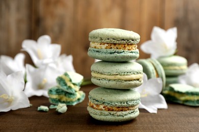 Photo of Delicious macarons and flowers on wooden table