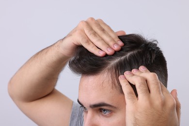 Man examining his head on light grey background, closeup. Dandruff problem