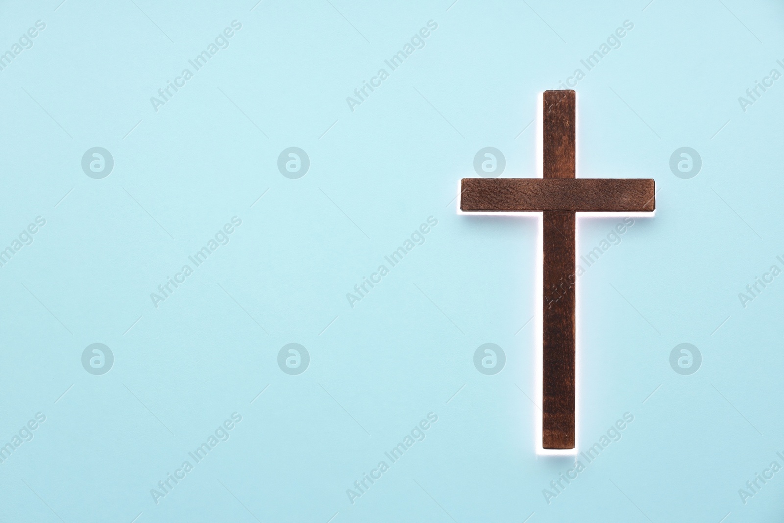 Photo of Shining cross on light blue background, space for text. Religion of Christianity