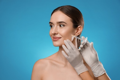 Photo of Beautiful woman getting facial injection on light blue background. Cosmetic surgery