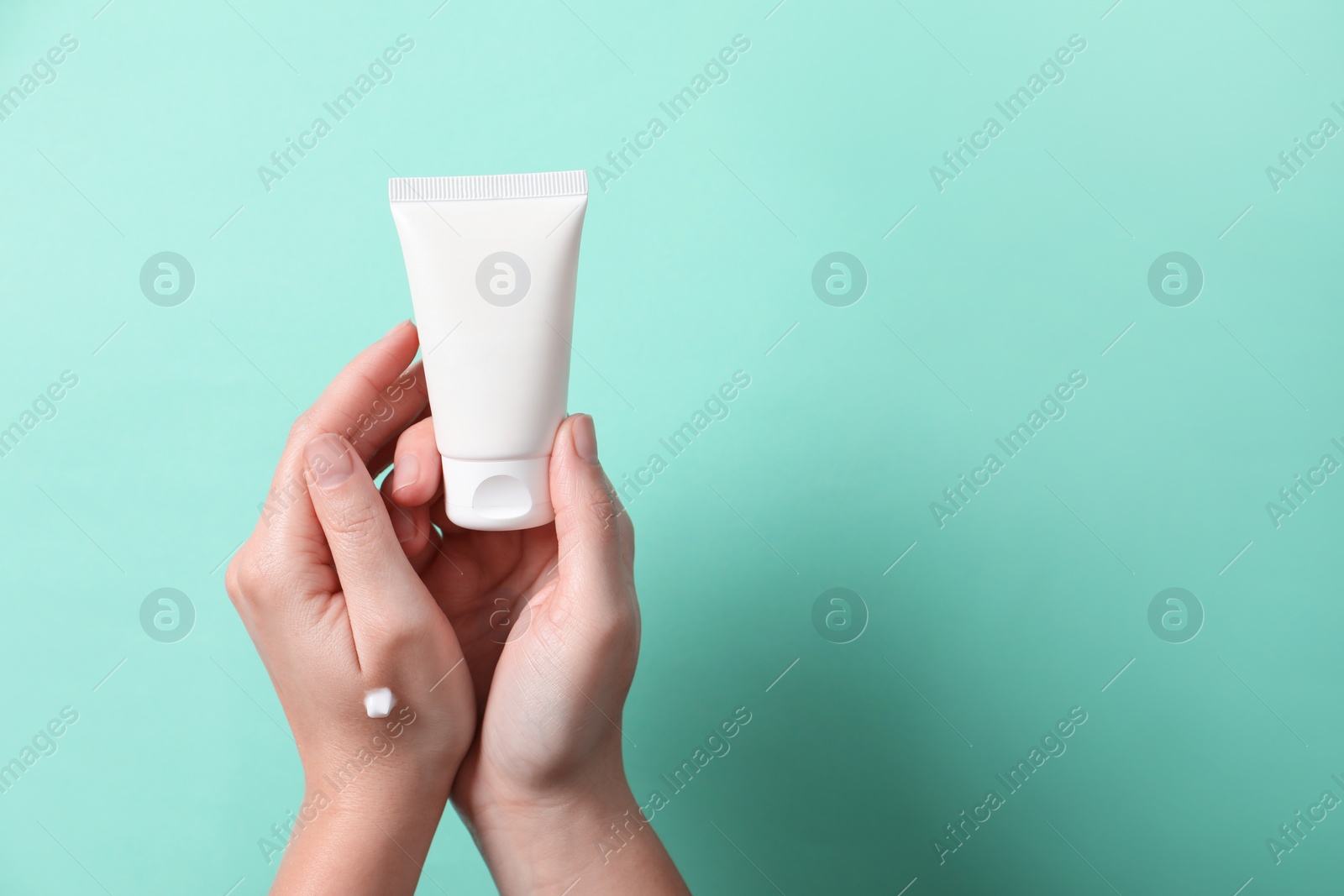 Photo of Woman with tube of hand cream on turquoise background, closeup. Space for text