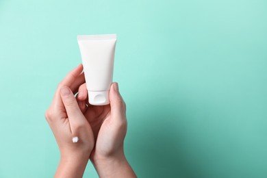 Woman with tube of hand cream on turquoise background, closeup. Space for text