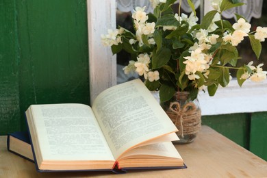 Photo of Books and beautiful jasmine flowers on wooden table near window outdoors