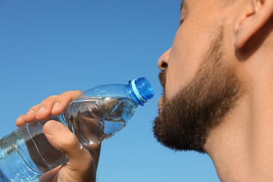 Man drinking water against blue sky on hot summer day, closeup. Refreshing drink