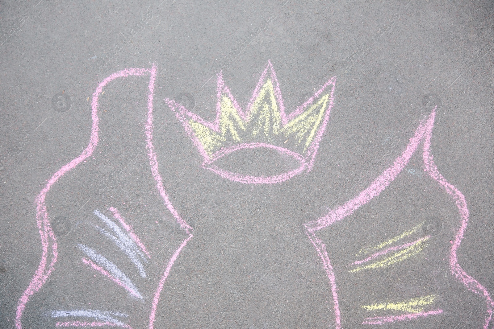 Photo of Child's chalk drawing of crown and wings on asphalt, top view