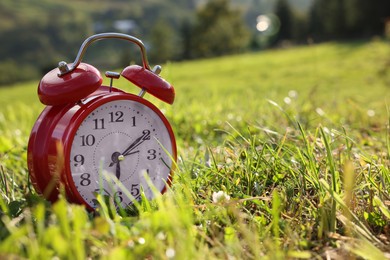 Photo of Red alarm clock on green meadow in morning