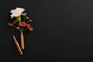 Bullet and cartridge case with beautiful flowers on black background, flat lay. Space for text
