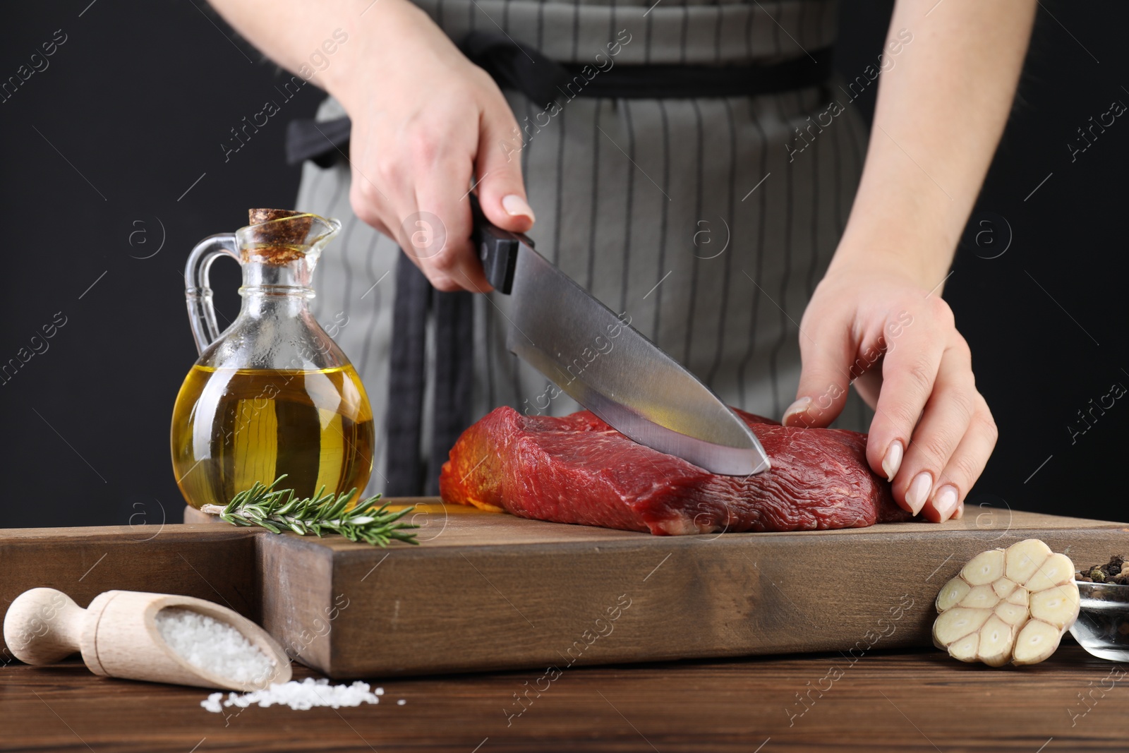 Photo of Woman cutting fresh raw beef steak at wooden table, closeup