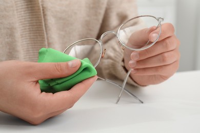 Woman wiping her glasses with microfiber cloth at white table, closeup