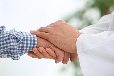 Photo of Doctor holding elderly patient hand on blurred background, closeup