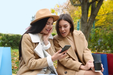 Special Promotion. Emotional young women with smartphone and shopping bags in park