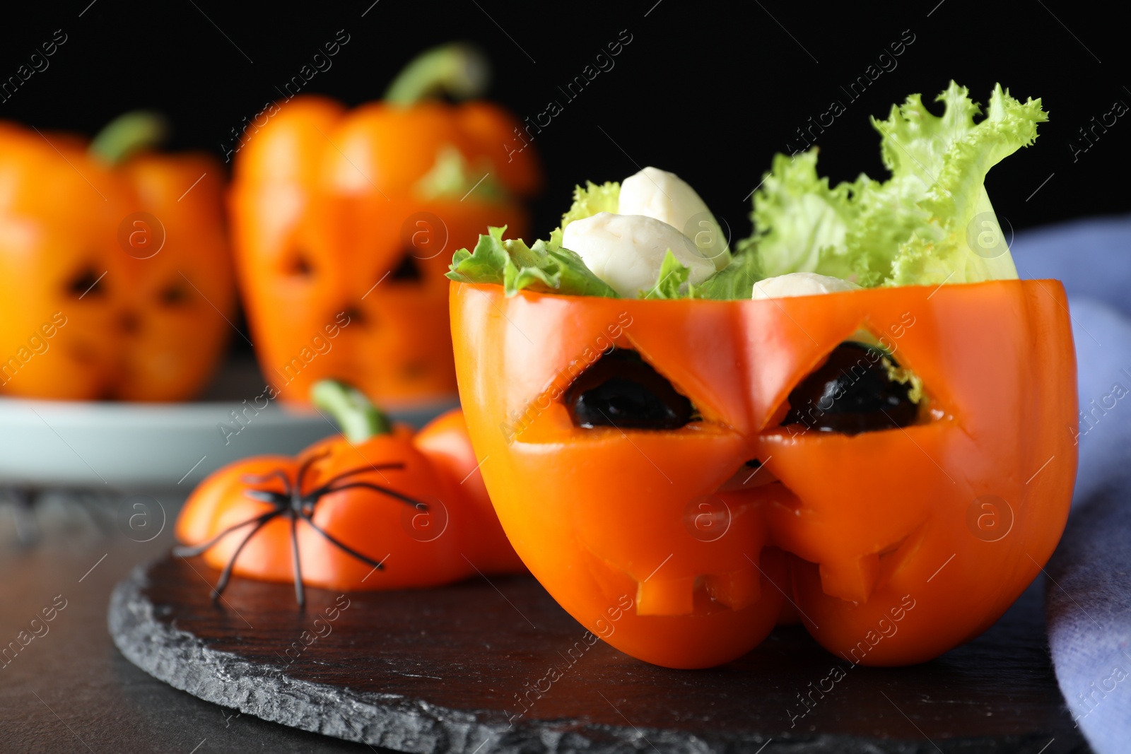 Photo of Bell pepper with black olives, mozzarella and lettuce as Halloween monster on dark table, closeup