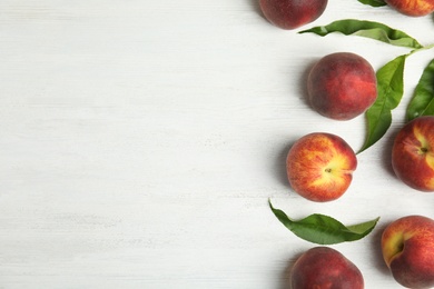 Photo of Fresh peaches and leaves on white wooden table, flat lay. Space for text