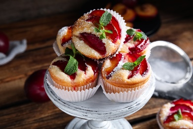 Photo of Delicious sweet cupcakes with plums on wooden stand, closeup
