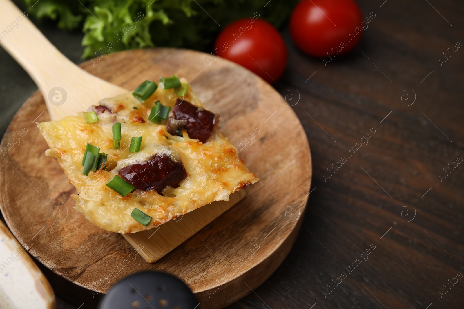 Photo of Spatula with piece of tasty sausage casserole on wooden table, closeup. Space for text