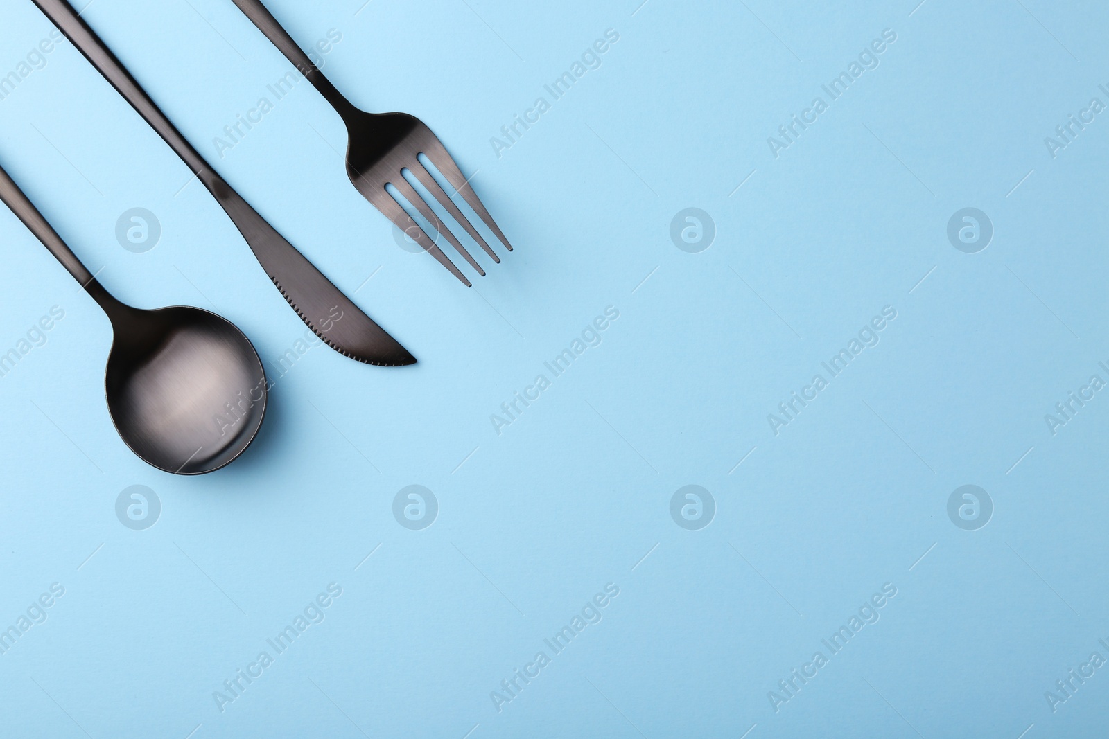 Photo of Stylish cutlery set on light blue table, flat lay. Space for text