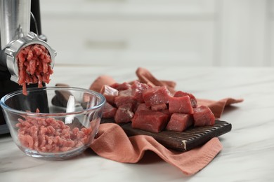 Photo of Electric meat grinder with beef mince on white table against blurred background, closeup. Space for text