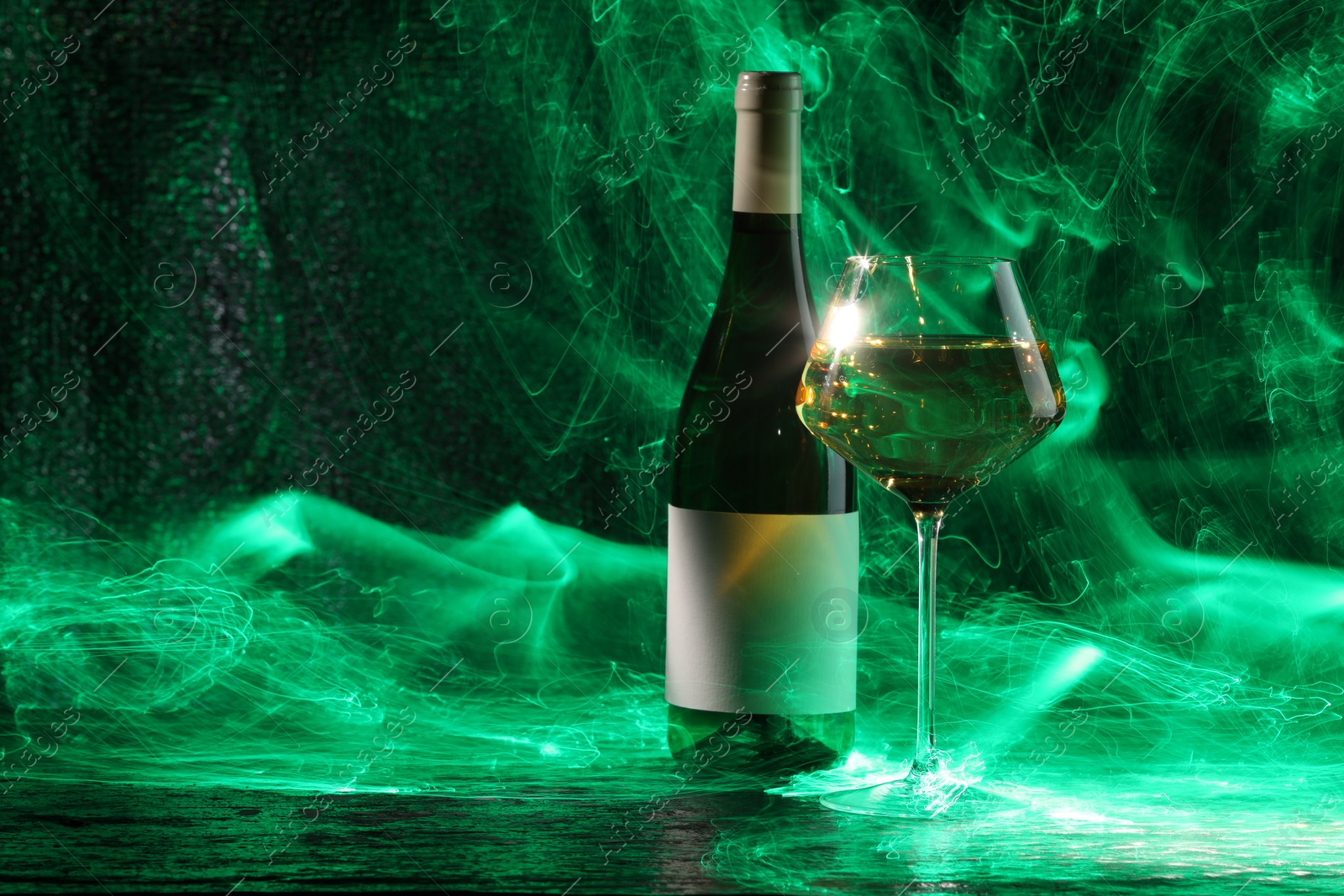 Photo of White wine in glass and bottle in green lights, space for text