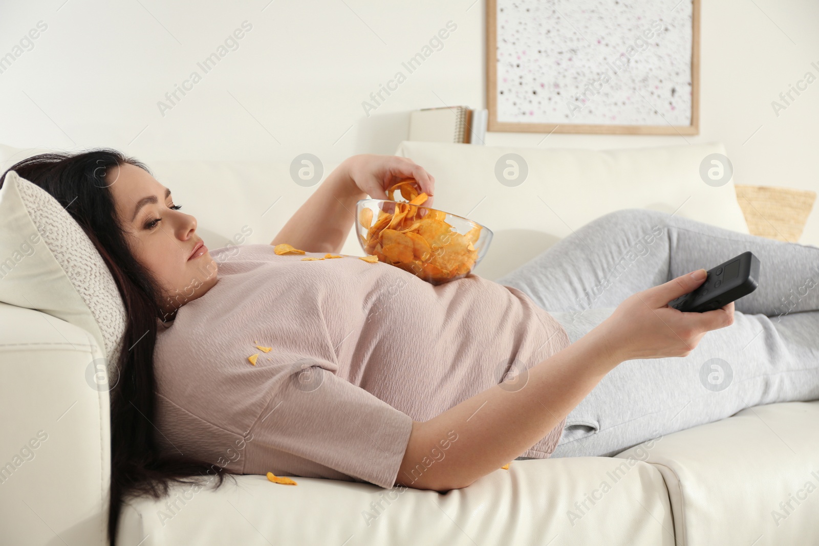 Photo of Lazy overweight woman with chips watching TV on sofa at home