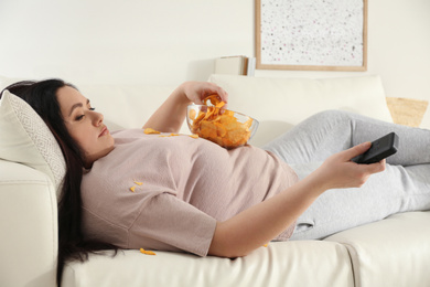 Photo of Lazy overweight woman with chips watching TV on sofa at home