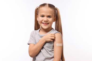 Photo of Happy girl with sticking plaster on arm after vaccination against white background