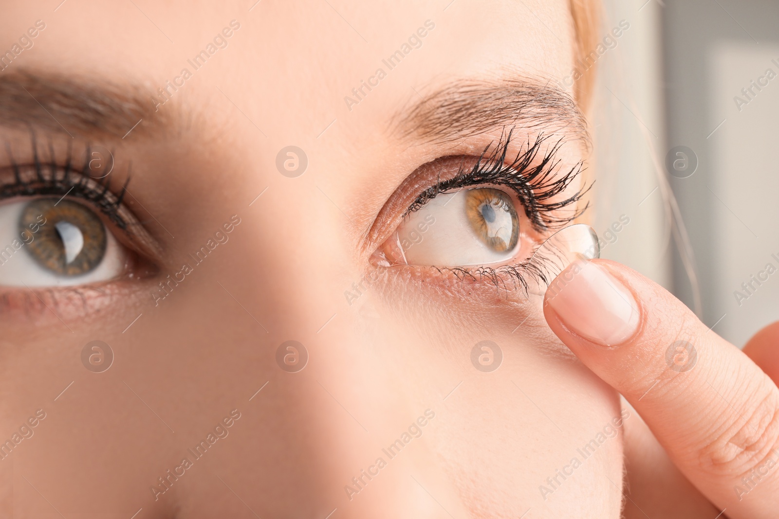 Photo of Young woman putting contact lens in her eye, closeup