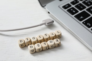 Photo of Cubes with words DIGITAL DETOX and disconnected charging cable on white wooden background