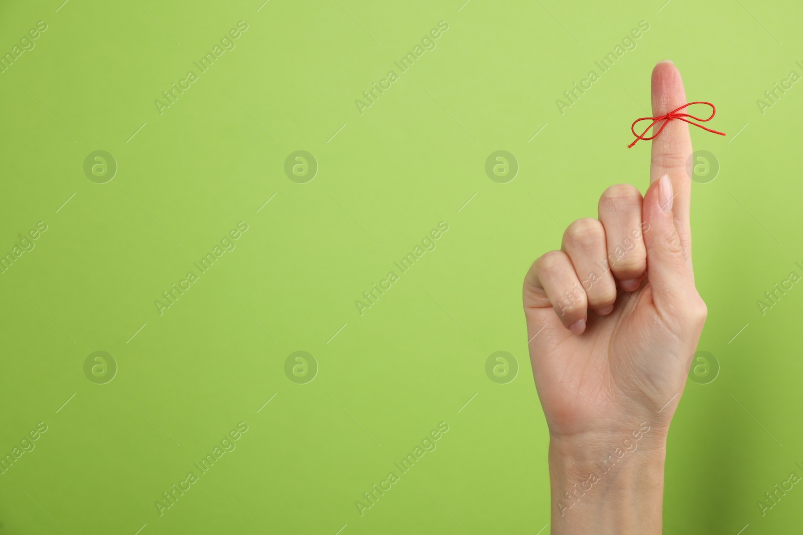 Photo of Woman showing index finger with tied red bow as reminder on light green background, closeup. Space for text