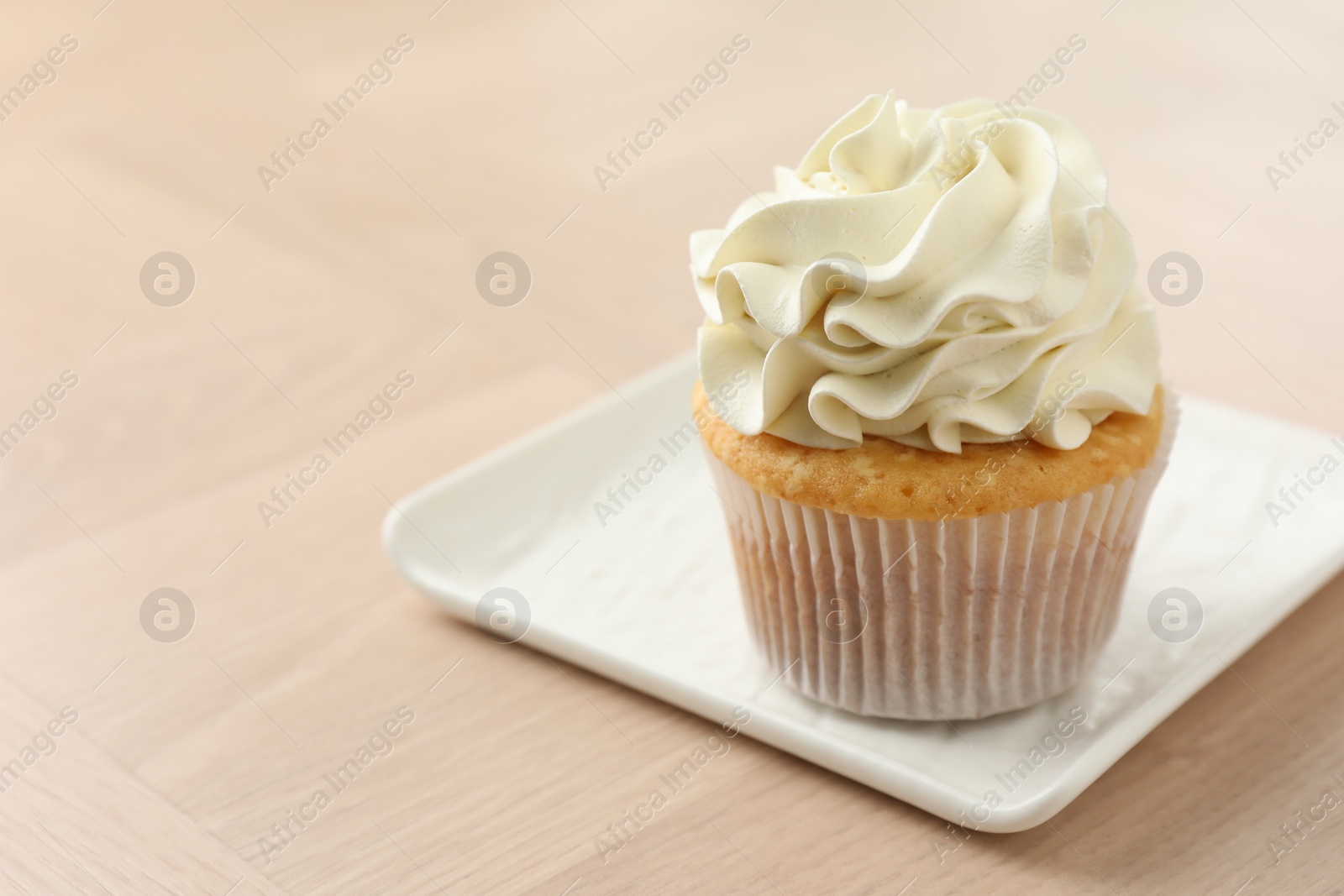 Photo of Tasty cupcake with vanilla cream on light wooden table, closeup. Space for text