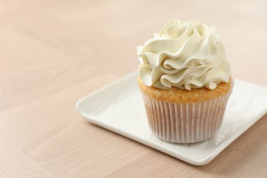 Photo of Tasty cupcake with vanilla cream on light wooden table, closeup. Space for text