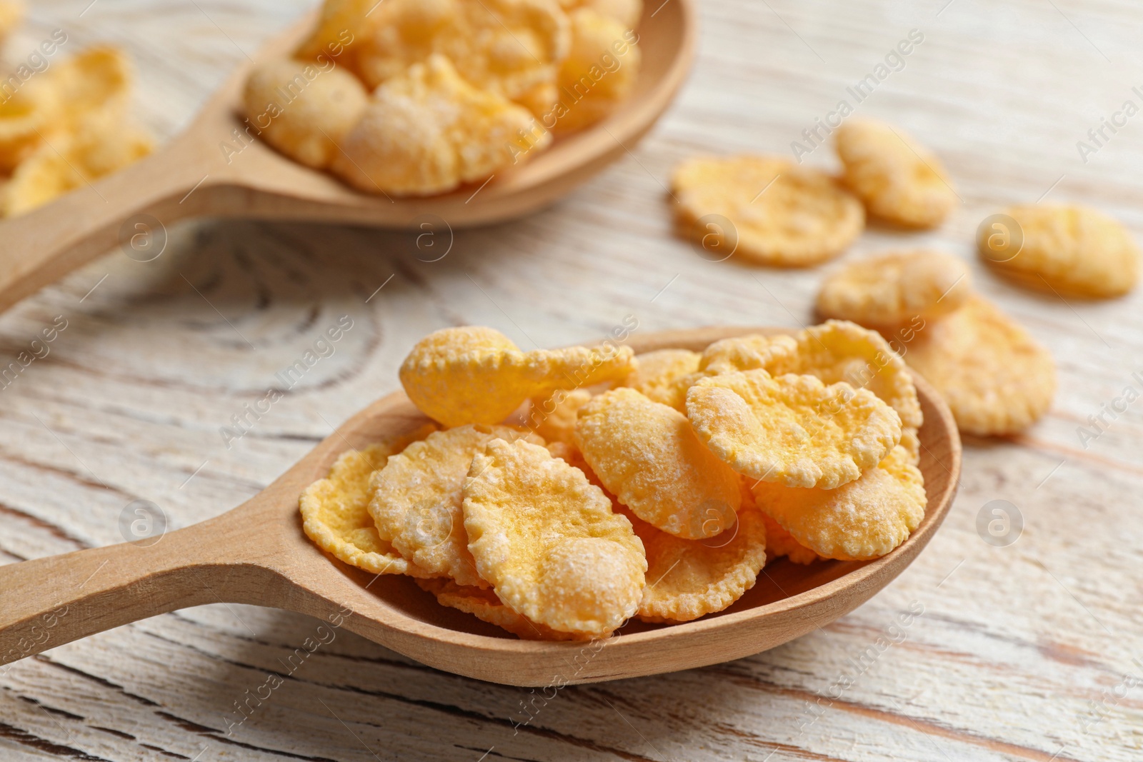 Photo of Two spoons and tasty corn flakes on white wooden table, closeup