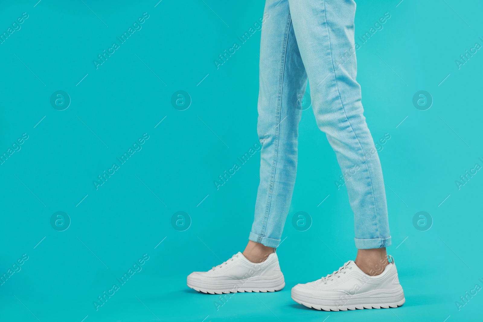 Photo of Woman in stylish sport shoes on light blue background. Space for text