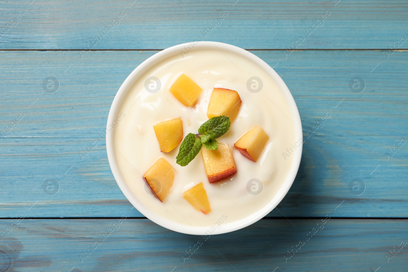 Photo of Delicious yogurt with fresh peach and mint on light blue wooden table, top view