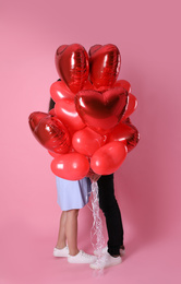 Photo of Lovely couple hiding behind heart shaped balloons on pink background. Valentine's day celebration