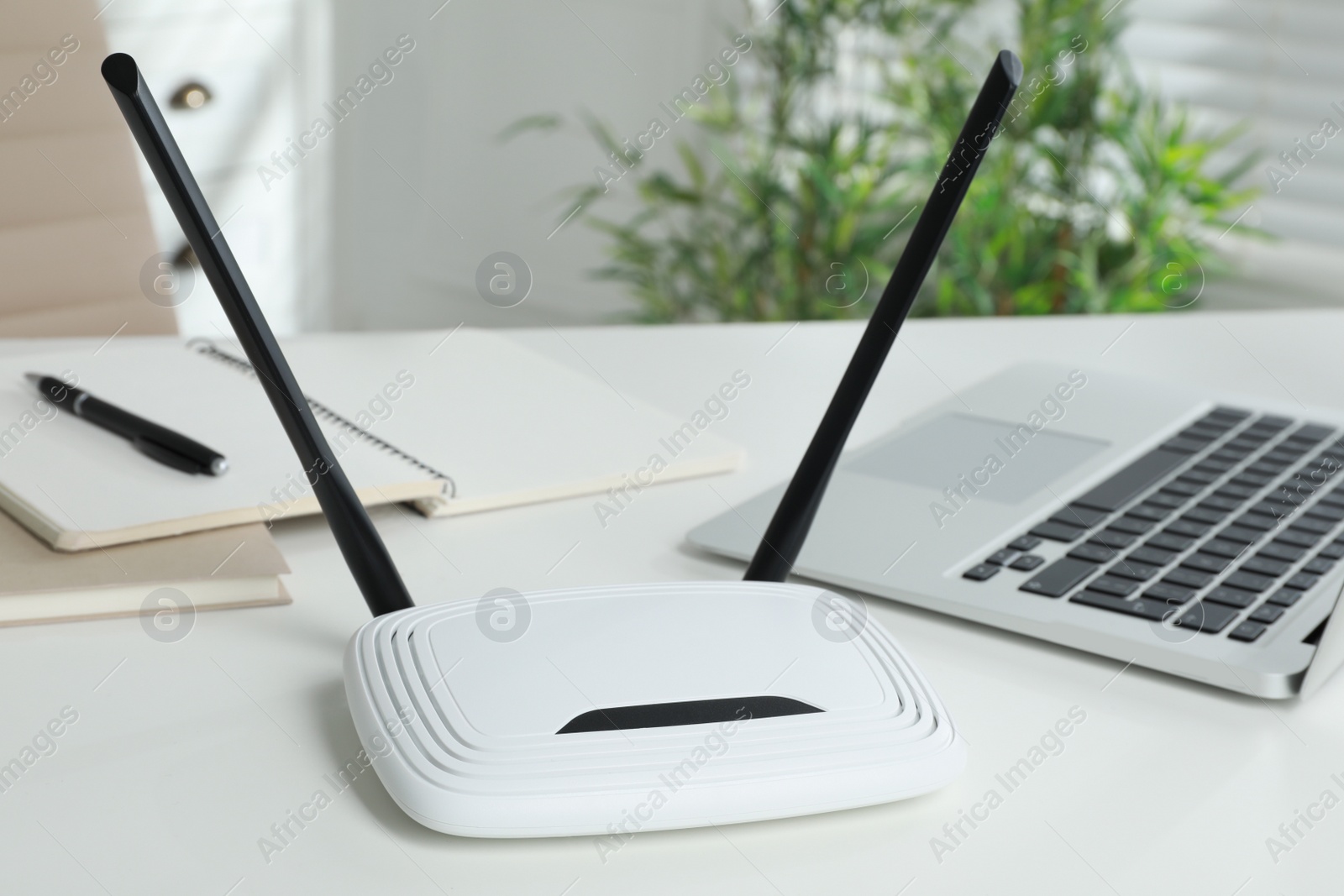 Photo of Modern wi-fi router and laptop on white table indoors