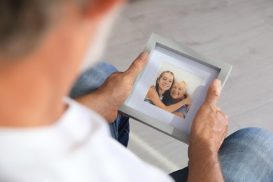Photo of Senior man holding frame with photo of his wife and granddaughter at home, closeup