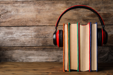 Books and modern headphones on wooden table. Space for text