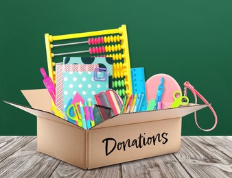 Image of Donation box with different school stationery on wooden table near chalkboard