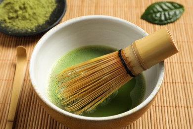 Photo of Cup of fresh green matcha tea with whisk and spoon on bamboo mat, closeup
