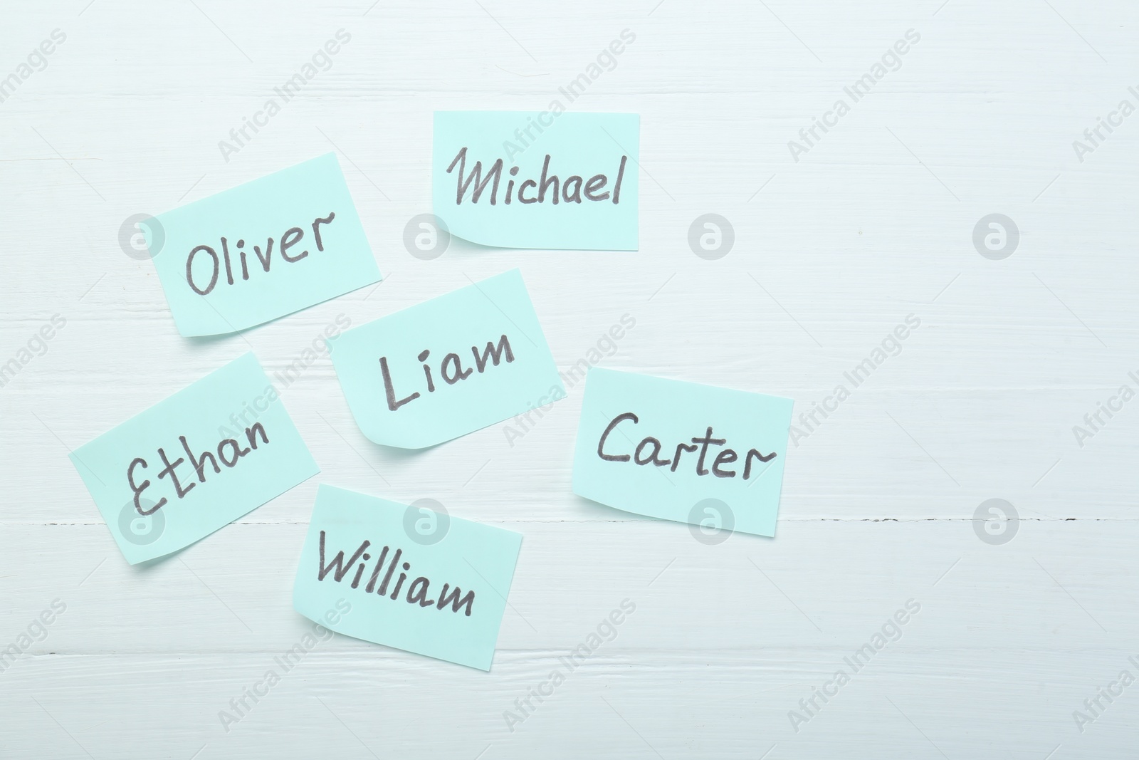 Photo of Paper stickers with different names on white wooden background, flat lay. Choosing baby's name