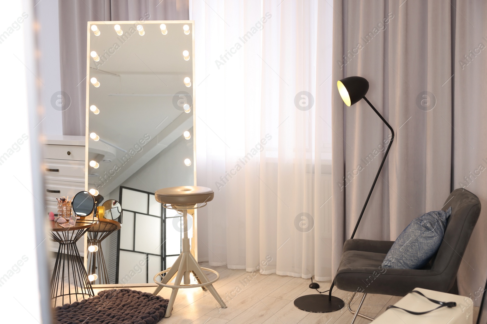 Photo of Makeup room. Stylish mirror with light bulbs, beauty products on table and chair indoors
