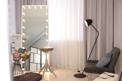 Photo of Makeup room. Stylish mirror with light bulbs, beauty products on table and chair indoors