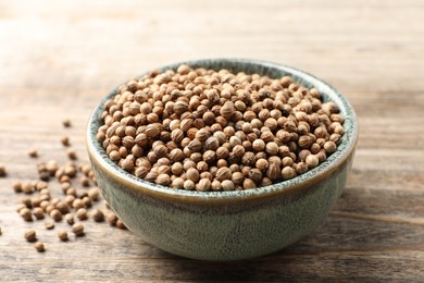 Dried coriander seeds in bowl on wooden table, closeup