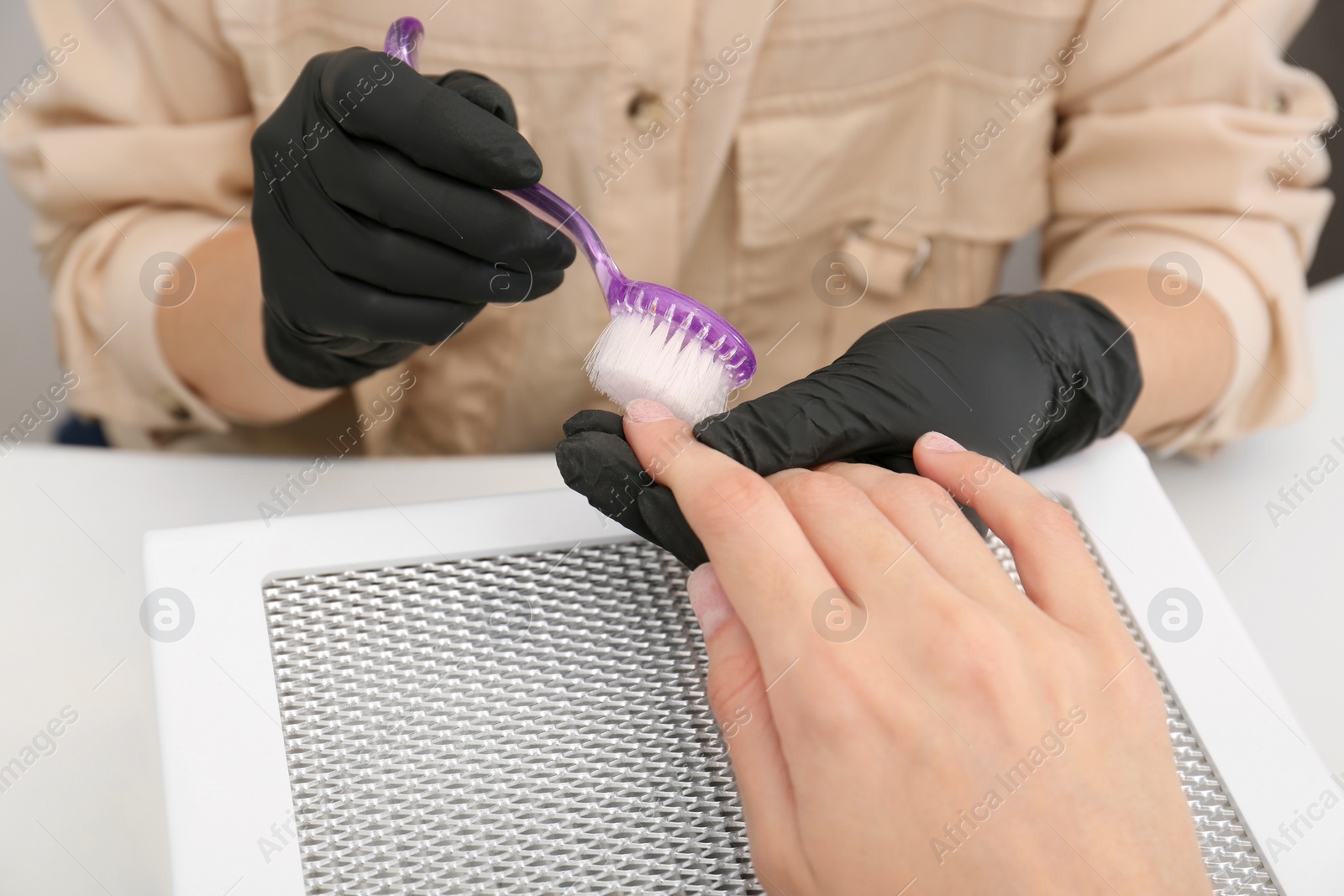 Photo of Professional manicurist working with client at white table, closeup