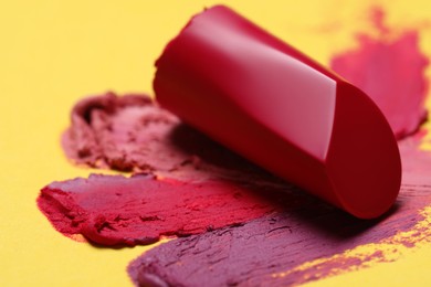 Photo of Bright lipstick and different smears on yellow background, closeup