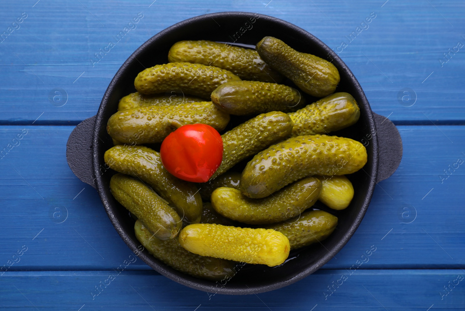 Photo of Serving pan with pickled cucumbers and pepper on blue wooden table, top view