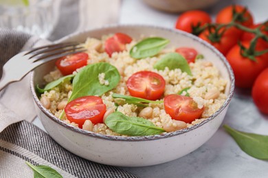 Photo of Delicious quinoa salad with tomatoes, beans and spinach leaves served on white marble table, closeup