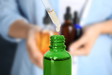 Image of Little bottle with essential oil and dropper against blurred background